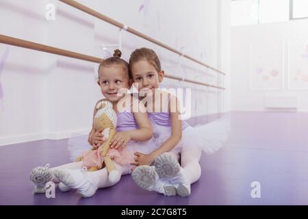Schöne glückliche kleine Mädchen tragen Ballett-Tanz-Outfits lächeln an der Kamera, sitzen auf dem Boden in der Ballettschule, kopieren Raum Stockfoto