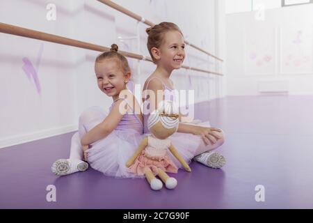 Schöne kleine Ballerinas, die sich nach dem Tanzen im Ballettunterricht entspannen und sich zurück an den Rücken lehnen. Fröhliche kleine Ballerinas lächeln freudig, Spaß am Tanz s Stockfoto