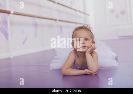 Kleine niedliche Ballerina Mädchen auf dem Boden in der Ballettschule liegen, müde aussehen, kopieren Raum. Liebenswert kleine Ballerina in Tutu Rock, suchen traurig und ti Stockfoto