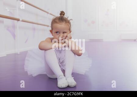 Liebenswert kleines Mädchen Ballerina suchen mürrisch, allein auf dem Boden sitzen in der Ballettschule, kopieren Raum. Niedliche kleine Ballerina suchen gelangweilt und ärgern Stockfoto