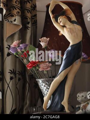 Vertikale Aufnahme einer Statue eines Weibchens in der Nähe eines Vase mit Blumen und Lampe Stockfoto