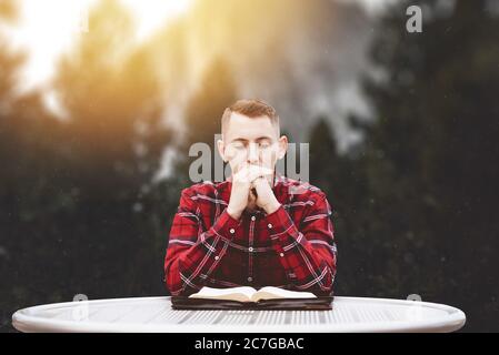 Weißer Mann trägt ein rotes Flanellhemd und betet unter dem Strahlende Sonnenstrahlen Stockfoto