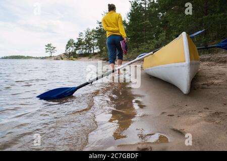 Frau, die am Sandstrand in der Nähe des Kajaks spazieren geht. Stockfoto