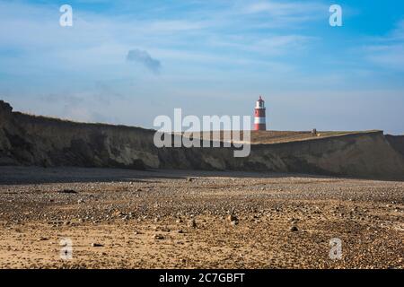 Norfolk Beach, Blick auf erodierte Klippen am Strand von Happisburgh, wo der Leuchtturm und die Menschen auf dem North Norfolk Coastal Path, Großbritannien, zu Fuß zu sehen sind Stockfoto