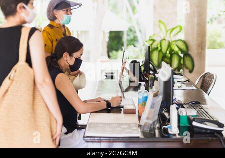 Eine Kundin, die im Hotel nachcheckt, trägt eine medizinische Maske gegen Viren. Stockfoto