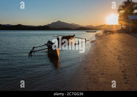 Blick auf die Küste der Nosy Komba Insel mit einem traditionellen Holzboot am Strand bei Sonnenuntergang, Nosy Komba, Madagaskar Stockfoto