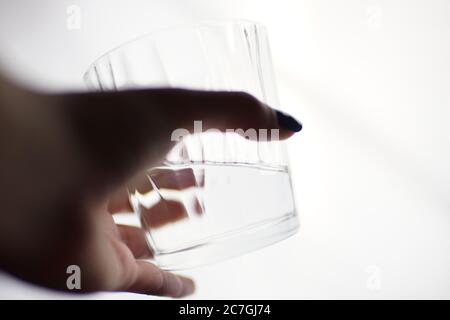Ein Glas Wasser in einer weiblichen Hand auf einem weißen isolierten Hintergrund. Seitenansicht, selektiver Fokus. Stockfoto