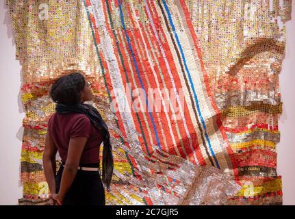 London, Großbritannien. 17. Juli 2020. Fokus auf El Anatsui Ausstellung in der October Gallery läuft vom 15. Juli - 8. August 2020 zeigt Metallarbeiten und eine Auswahl von Grafiken in Zusammenarbeit mit Factum Arte, Madrid. El Anatsui ist heute vor allem für seine Werke bekannt, die aus vielen tausend Aluminium-Flaschenverschlüsse bestehen. Galeriemanager Saara studiert Installation Change in Fortune, 2018, Aluminium und Kupfer. Quelle: Malcolm Park/Alamy Live News. Stockfoto