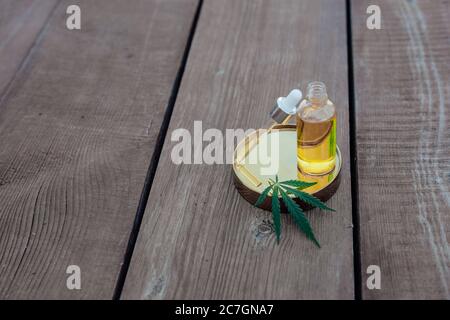 Glasflasche und Tropferöl CBD, THC-Tinktur und Cannabisblatt auf Holzhintergrund. Laborproduktion von Kosmetika mit CBD-Öl. Stockfoto