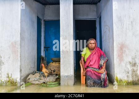 Bogura, Bangladesch. Juli 2020. Eine Frau sitzt vor ihrem überfluteten Haus in Bogura.ein Drittel von Bangladesch ist unter Wasser, nachdem schwere Regenfälle die Nation getroffen haben. Mindestens 1.5 Millionen Menschen sind betroffen, Häuser und Straßen in Dörfern überschwemmt. Beamte des Hochwasserprognosen- und Warnzentrums (FFWC) haben berichtet, dass die Hochwassersituation in 15 nördlichen und zentralen Bezirken auf den Anstieg der Wasserstände der Hauptflüsse zurückzuführen ist, einschließlich der Brahmaputra, Jamuna, Padma, Teesta und Dharla. Kredit: SOPA Images Limited/Alamy Live Nachrichten Stockfoto