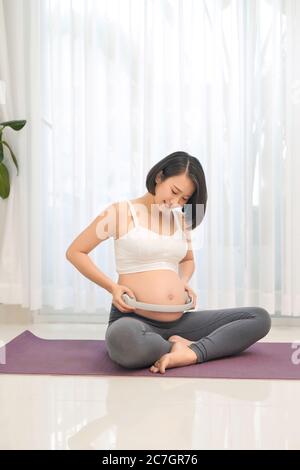 Schwangere Frau hält Kopfhörer auf ihrem Bauch im Wohnzimmer Stockfoto