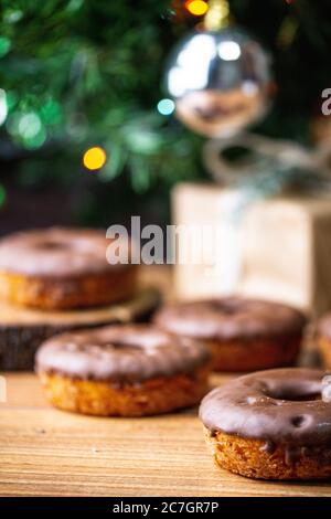 Vertikaler selektiver Fokus von Donut vor Unschärfen Geschmückter Weihnachtsbaum und Donuts Stockfoto