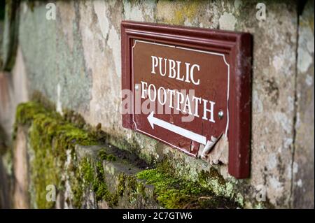 Ein altes, verzweifeltes öffentliches Wegzeichen auf einer moosbedeckten alten Steinmauer. Stockfoto