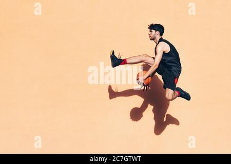 Basketballspieler springt mit dem Ball in den Händen vor einer Wand Stockfoto