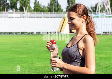 Schöne Frau trinkt Wasser und hört die Musik auf Kopfhörern im Stadion. Mädchen hat nach dem Training eine Pause. Stockfoto