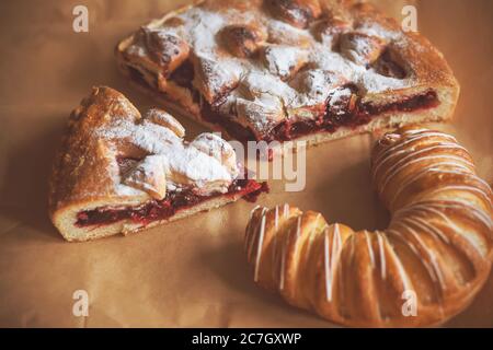 Köstliche süße Backwaren auf Geschenkpapier. Kirschkuchen und ein Bagel mit Zuckerguss. Hausmannskost. Stockfoto