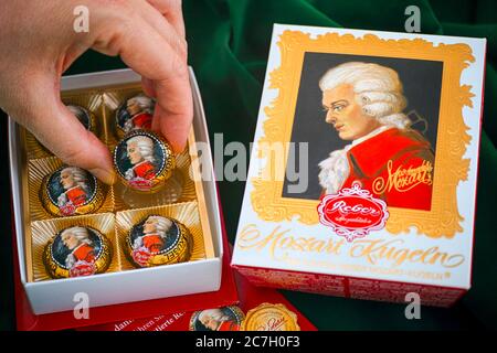 Tambow, Russische Föderation - 14. Februar 2020 Person Hand nehmen Mozart Süßigkeiten aus Süßigkeiten-Box. Grüner Samthintergrund. Stockfoto