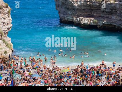 Polignano a Mare, Italien - 15. August 2014: Menschen entspannen und schwimmen am schönen Strand Lama Monachile. Weiße Kiesbucht zwischen Felswänden und Fledermaus Stockfoto