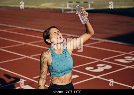 Müde Athlet Mädchen in Sportkleidung gießen frisches Wasser auf sich selbst nach dem Laufen auf Stadion Stockfoto