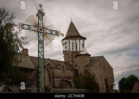 Nasbinals Kirche mit ornamentalem Kreuz im Vorgrund, bewölkt, Lozere, Frankreich. Stockfoto