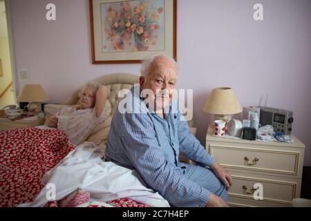 Ein älteres Paar in den 80ern saß auf dem Bett in ihrem Schlafanzug, bevor es morgens aufstand, England, Vereinigtes Königreich Stockfoto