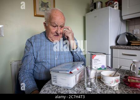 Älterer Mann in den 80ern, der seine Medikamente nahm, während er morgens am Frühstückstisch saß, England, Vereinigtes Königreich Stockfoto