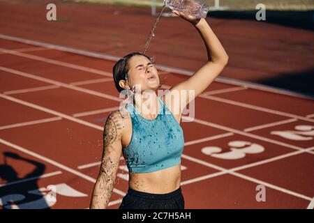 Müde sportliche Mädchen in Top Gießen frisches Wasser auf sich selbst nach dem Training im Stadion Stockfoto