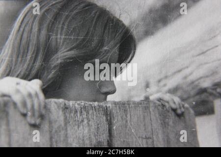 Schöne Schwarz-Weiß-Fotografie einer jungen Dame aus den 1970er Jahren, die über einen Holzzaun schaut. Stockfoto