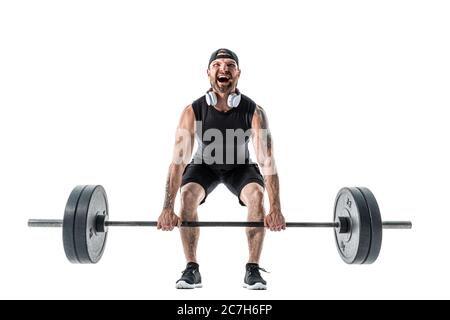 Aggressiver bärtiger starker muskulöser Mann in Sportbekleidung und Kopfhörern, der eine Deadlift-Übung macht. Ganzkörperaufnahme isoliert auf Weiß. Stockfoto