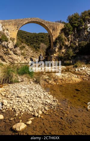 Europa, Spanien, Katalonien, Provinz Gerona, La Garrotxa, Montagut, Wanderer blickt auf die mittelalterliche Brücke über den Llierca Fluss Stockfoto