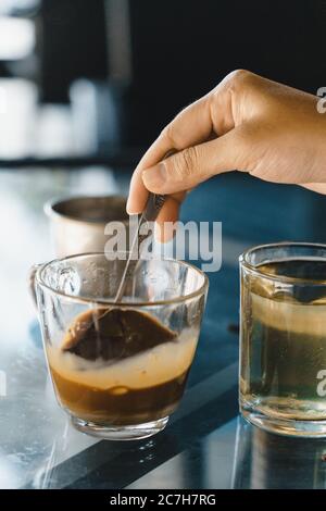 Nahaufnahme Hände einer Frau Rühren Kaffee, heiße Milch Kaffee tropft in Vietnam-Stil. Selektiver Fokus. Getränke- und Reisekonzept Stockfoto