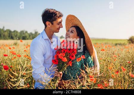 Liebevolles Paar umarmt in Mohn Feld mit Blumenstrauß. Glücklicher Mann und Frau, die Spaß haben. Sommerurlaub Stockfoto