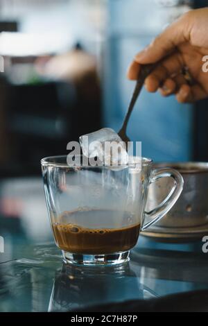 Nahaufnahme Hände einer Frau Rühren Kaffee, heiße Milch Kaffee tropft in Vietnam-Stil. Selektiver Fokus. Getränke- und Reisekonzept Stockfoto