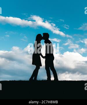 Silhouette von Mann und Frau küssen gegen einen blauen Himmel mit Wolken. Stockfoto