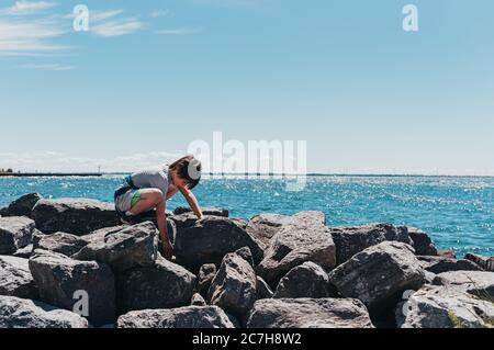 Junge hocken an der felsigen Küste eines Sees an einem sonnigen Sommertag. Stockfoto