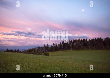 Pastellrosa Sonnenuntergang Wolkenlandschaft über dem Jura-Gebirge. Schöne Abendhimmellandschaft über Wiesen und Wald. Stockfoto