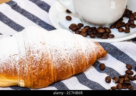 Blätterteig, Kaffeetasse und gebuttertes französisches Croissant auf Holzkiste. Speisen- und Frühstückskonzept. Details zu Kaffeedesserts und frischem Gebäck Stockfoto