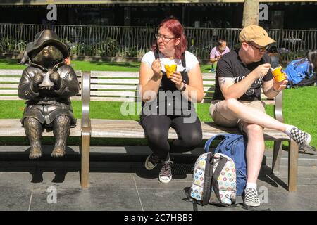 London, Großbritannien. Juli 2020. Die Leute genießen eine Erfrischung neben der Statue des Paddington Bären am Leicester Square. Das West End wird langsam geschäftiger, wenn die Menschen in die Geschäfte und Parks im Zentrum Londons in der Sonne zurückkehren. Kredit: Imageplotter/Alamy Live Nachrichten Stockfoto