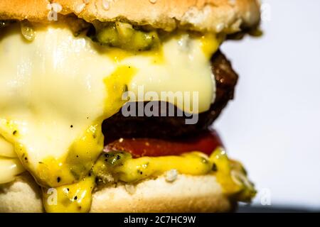 Nahaufnahme von geschmolzenem Käse in einem hausgemachten Cheeseburger isoliert auf schwarzem Teller. Stockfoto