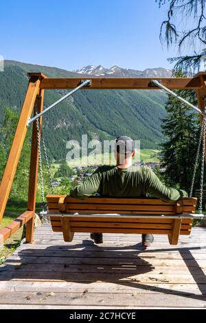 Europa, Österreich, Tirol, Ötztal Alpen, Ötztal, Wanderer sitzt auf einer Schaukel und blickt auf das Bergdorf Niederthai Stockfoto