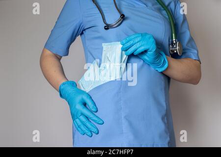 Ein Arzt in einer medizinischen Maske und blauer Uniform hält viele medizinische Schutzmasken. Stockfoto