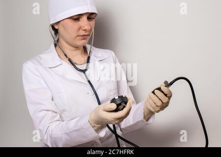 Ein Arzt in einer medizinischen Kappe und Uniform, ein Kardiologe misst den Blutdruck mit einem Blutdruck-Monitor. Herzerkrankungen, arterielle Hypertonie. Stockfoto