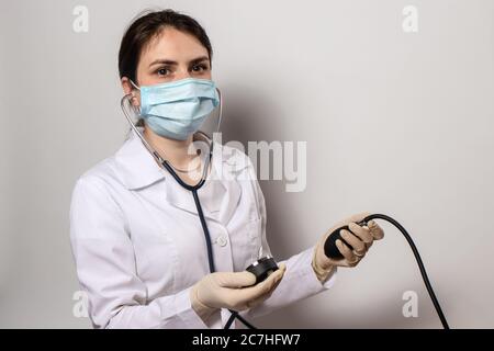 Arzt in einer medizinischen Maske misst der Kardiologe den Blutdruck mit einem Blutdruckmessgerät. Stockfoto