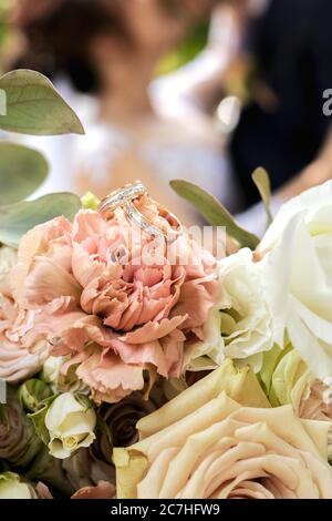 Goldene Eheringe auf dem Brautstrauß aus rosa, gelben und weißen zarten Rosen. Stockfoto