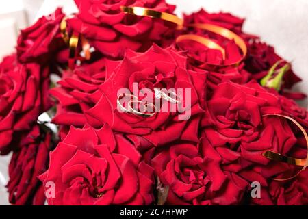 Goldene Eheringe auf einem Strauß roter Rosen Stockfoto