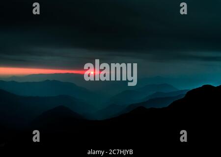 Eine Landschaft aus Hügellagen mit der untergehenden Sonne im Hintergrund und dunklem bewölktem Himmel darüber Stockfoto