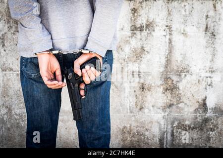 Nahaufnahme Hände gefesselt Handschellen und halten Waffe in hinter seinem Körper. Der verhaftete Mann legte Hände auf den Rücken. Stockfoto