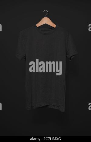Schwarzes T-Shirt auf einem Kleiderbügel vor schwarzem Hintergrund Stockfoto