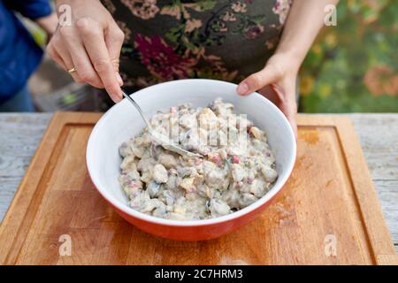 Weibliche Hände mit einem Löffel rühren Kastanienfruchtsalat in einer orangefarbenen Schüssel Stockfoto