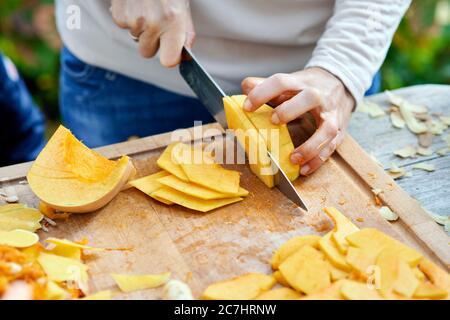 Eine halbe Hokkaido Kürbis und Kürbiskeile, auf einem Holzbrett mit einem Kochmesser gespalten Stockfoto